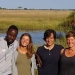 a group of people standing a front of a river between grassland