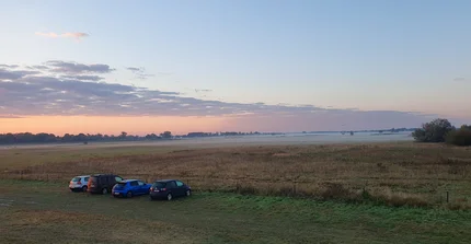 Die Wiesen, die Station umgeben, in einer morgendlichen Stimmung. Der Nebel steht tief und die Sonne geht auf.