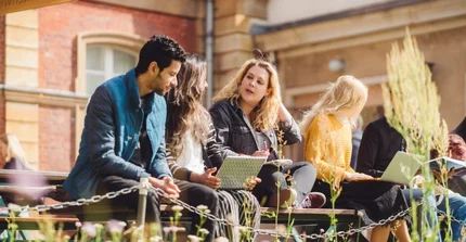 Studierende sitzen auf einer Bank am Campus Neues Palais und unterhalten sich. Eine Studentin hat einen Laptop auf dem Schoß.