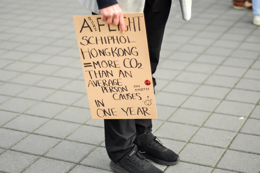 A man hold a protest sign about the environmental impact of a long-haul flight from Amsterdam to Hong Kong
