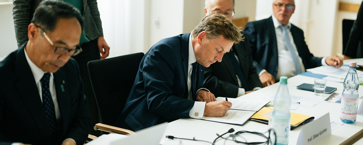 mehrere Männer, die an einem Tisch etwas unterschreiben - 