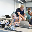 This image shows three students who are speaking with a lecturer in a seminar room.