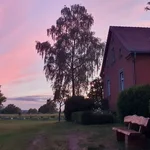 Eine Holzbank vor der Station wird vom indirekten Licht des Sonnenuntergangs beschienen. Der Himmel erstrahlt in warmen Pastelltönen.