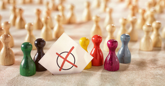 Verschieden farbige Spielfiguren symbolisieren verschiedene Wählerstimmen. Mittig im Bild ist ein Zettel mit einem roten Kreuz in einem Kreis, wie auf einem Wahlzettel.