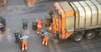 three man in orange clothes behind a garbidge collection truck