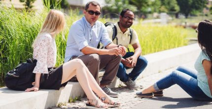 Students sit on a curb on Golm campus. A lawn can be seen behind them.
