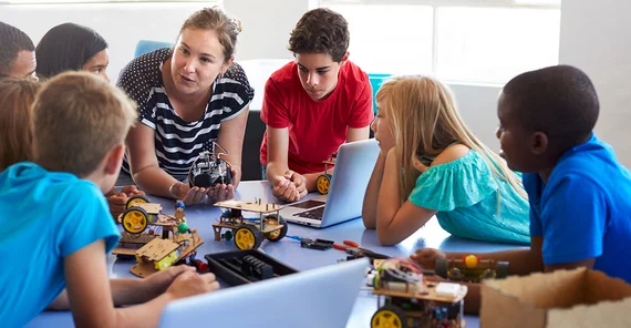 Kinder sitzen mit Lehrkraft an einem Tisch.