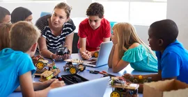 Kinder sitzen mit Lehrkraft an einem Tisch.