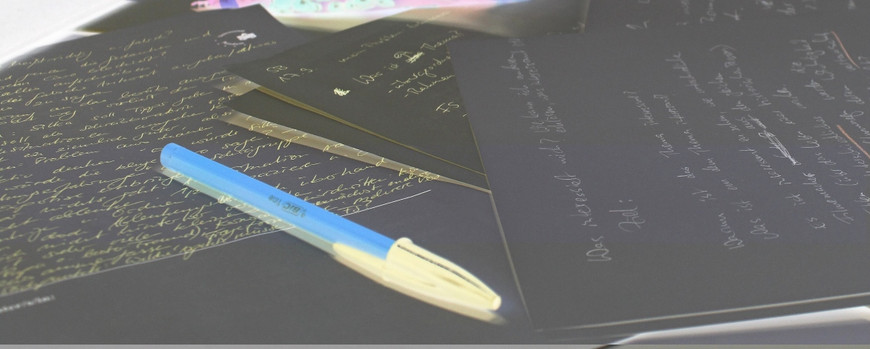 Mehrere beschriebene Blätter und ein quer darüberliegender Stift. Aufgrund der Negativ-Darstelung ist das Papier schwarz, die Schrift weiß, der Stift ist blau mit heller Kappe.