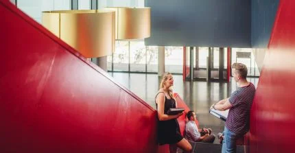 Eine Studentin und ein Student stehen in Haus 28 in Golm auf einer Treppe und unterhalten sich.