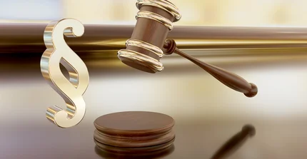 Denken Sie an eine Darstellung, die das Konzept von Recht und Gerechtigkeit symbolisiert. Im Vordergrund sehen Sie ein großes, glänzendes Zeichen – das ist das Paragraphen-Symbol, das aussieht wie ein doppeltes "S". Es ist aus goldglänzendem Metall gefertigt und wirkt sehr solide und wichtig. Daneben, leicht erhöht und schräg liegend, ist ein Richthammer zu sehen, auch "Gavel" genannt. Er hat einen runden Kopf und einen Griff, beides aus dunklem, poliertem Holz, und ist mit glänzenden, goldenen Bändern verziert, die ihn umschließen. Unter dem Hammer, direkt auf dem Boden, liegt eine kleine, runde Holzscheibe, auf die der Hammer normalerweise schlagen würde. Der gesamte Hintergrund ist weich und unscharf, in warmen Gold- und Brauntönen gehalten, die das glänzende Gold des Paragraphen-Symbols und des Hammers hervorheben. Das Bild vermittelt einen ernsten und offiziellen Eindruck, der mit juristischen Angelegenheiten oder Entscheidungen assoziiert wird.