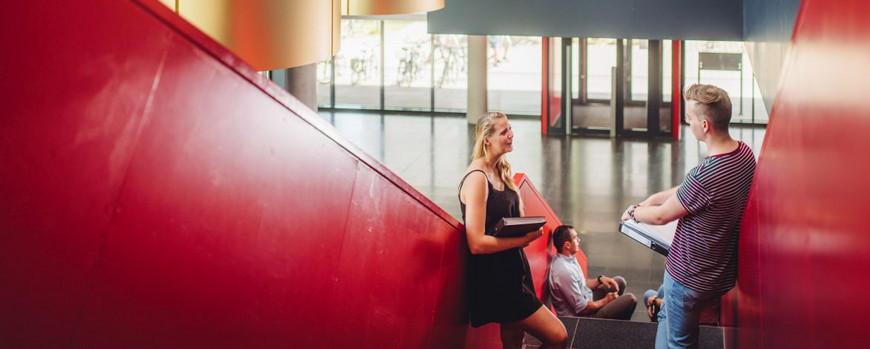 A female student and a male student standing on a staircase and talking in building 28 in Golm.