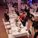 Tische mit weißen Tischdecken, an denen mehrere Personen sitzen.