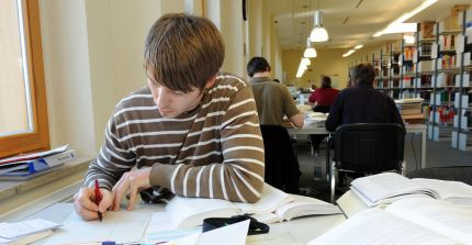 Studierender in der Bibliothek an einem Tisch mit augeschlagenen Büchern.