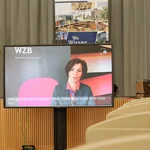 Jutta Allmendinger, Ph.D., Präsidentin des Wissenschaftszentrums Berlin für Sozialforschung gGmbH, in einer Videobotschaft auf einem Bildschirm vor der Bühne.