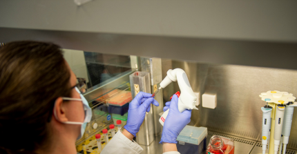 Frau mit Maske und Laborhandschuhe beim Pipettieren