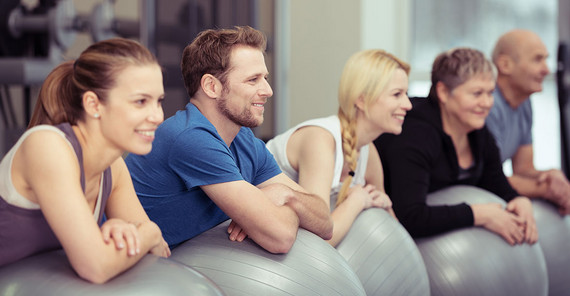 Eine Gruppe von Sportlerinnen und Sportlern lehnt auf einem Gymnastikball