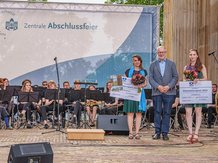 1 Mann und zwei Frauen bei der Preisverleihung, im Hintergrund ein Orchester