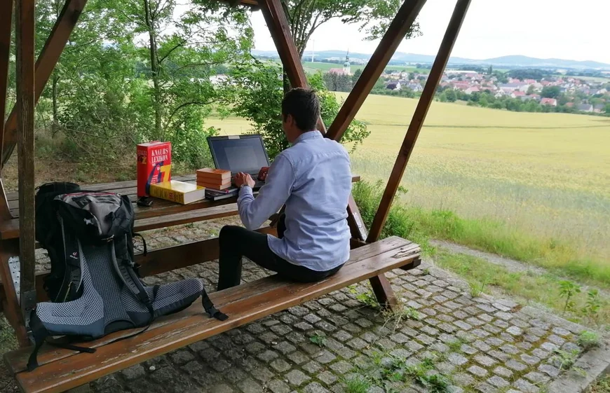 Mann auf Sitzgarnitur im Wald mit Laptop und Büchern