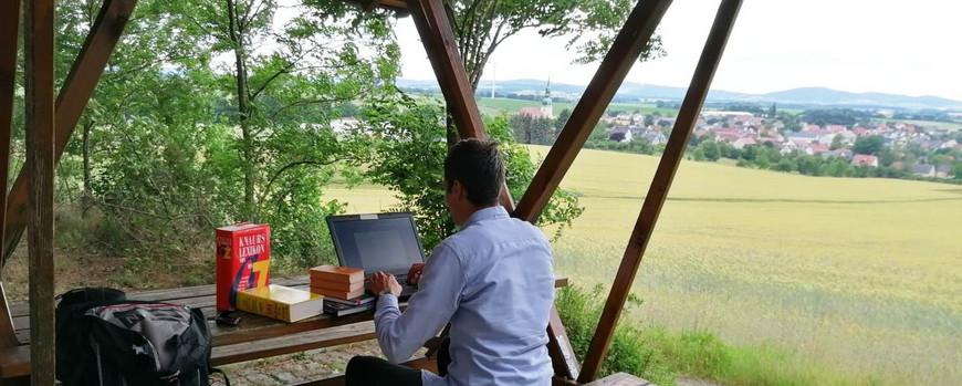 Mann auf Sitzgarnitur im Wald mit Laptop und Büchern