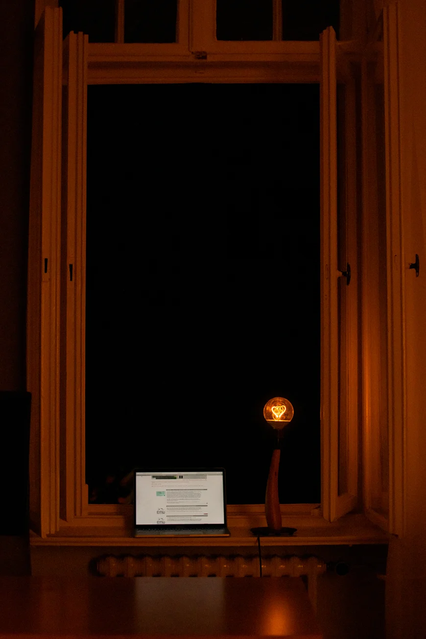 Laptop mit Lampe vor offenem Fenster in der Nacht