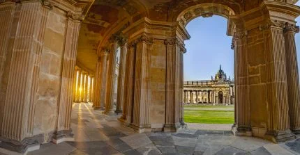 Blick aus einem halbrunden Säulengang auf ein historisches Nebengebäude des Neuen Palais