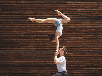 Ein Mann stemmt eine Frau nach oben, die auf seinen Händen einen Handstand macht