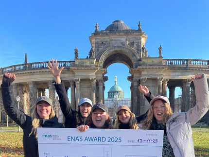 Das Team des Feel Good Campus steht vor den Kolonnaden des Neuen Palais und fällt den Check für den Enas Eward in den Händen