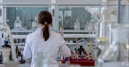 Scientist (photographed from behind with smock) in laboratory with many glass instruments and samples