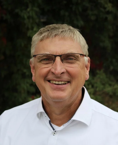 Auf der Porträt-Aufnahme ist Prof. Dr. Manfred Rolfes zu sehen. Er trägt ein weißes Hemd und eine Brille und lächelt.
