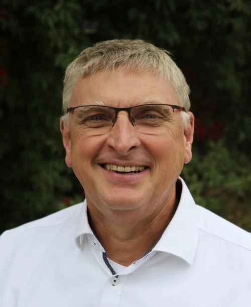 Auf der Porträt-Aufnahme ist Prof. Dr. Manfred Rolfes zu sehen. Er trägt ein weißes Hemd und eine Brille und lächelt.