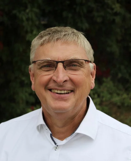 Auf der Porträt-Aufnahme ist Prof. Dr. Manfred Rolfes zu sehen. Er trägt ein weißes Hemd und eine Brille und lächelt.