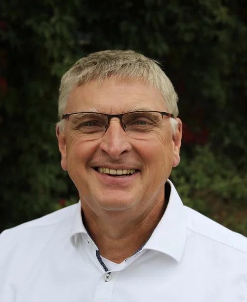 Auf der Porträt-Aufnahme ist Prof. Dr. Manfred Rolfes zu sehen. Er trägt ein weißes Hemd und eine Brille und lächelt.
