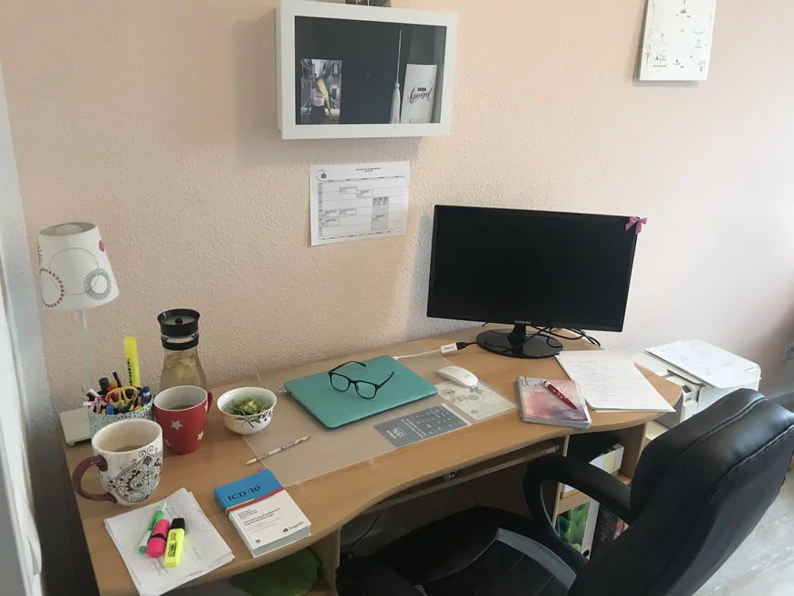 SChreibtisch mit Tassen, SChreibzeug, Brille, Lampe, Monitor