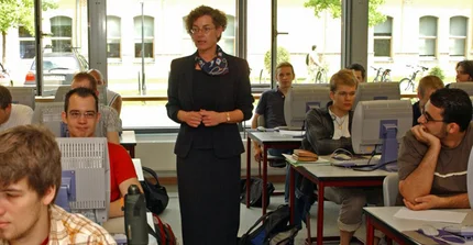 Lehrerin im Klassenraum mit Schülern hinter Computer-Bildschirmen