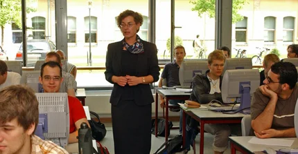 Lehrerin im Klassenraum mit Schülern hinter Computer-Bildschirmen