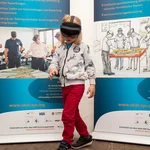 Ein Kind mit einer VR-Brille steht vor zwei Werbebannern