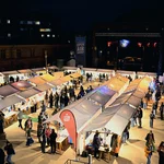 Erleuchtete Marktstände im Dunkeln; dazwischen Menschen