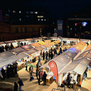 Erleuchtete Marktstände im Dunkeln; dazwischen Menschen