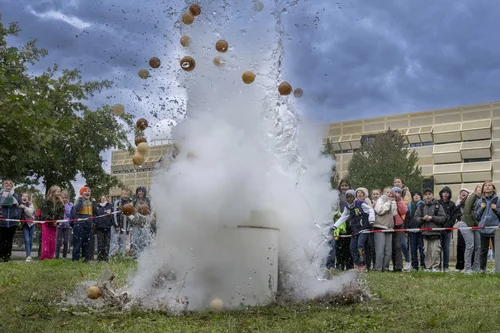 Der "Trash-Vulcano" bricht eindrucksvoll auf einer Wiese in Golm aus. Eine große Wasserfontäne spritzt in die Luft. Im Hintergrund staunende und überrascht schreiende Kinder.