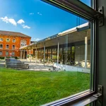 Bänke und Tische der Mensa, dahinter die Mensa und ein angrenzendes Haus