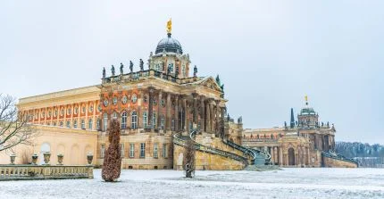 two historical buildings at Neues Palais behind snowy meadows