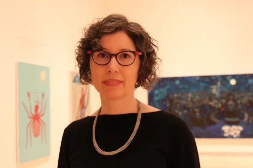 Sarah Casteel, wearing glasses and a necklace, stands in an office.