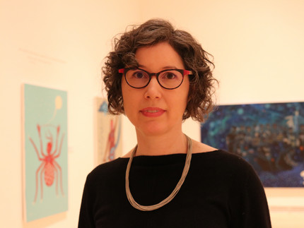 Sarah Casteel, wearing glasses and a necklace, stands in an office.