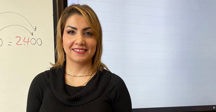 Entisar Karkoli in front of a blackboard.
