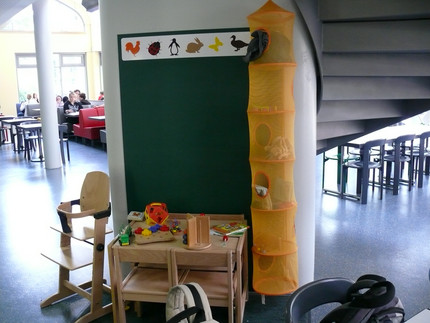 Eine Ecke mit Spielzeug, einem kleinen Tisch und zwei Stühlen für Kinder, einem Hochstuhl und einer Tafel.