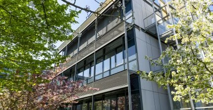 Fassade aus Stahl und Glas eines Forschungsgebäudes, davor zwei Bäume