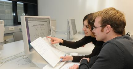 Two people talking in front of a PC