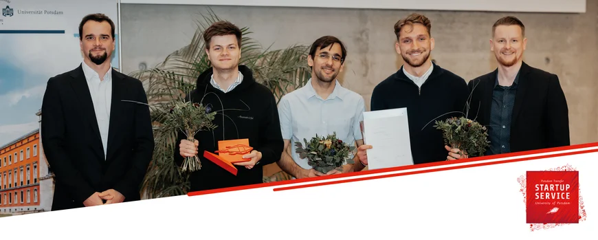 Fünf Männer in Anzügen mit Blumen und Urkunden