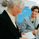 Zwei Frauen auf einem Podium, eine hält ein Mikrofon in der Hand